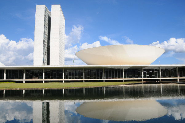 Fachada do edifício do Congresso Nacional em Brasília: cúpula do Senado, torres da Câmara dos Deputados e reflexo no espelho d'água